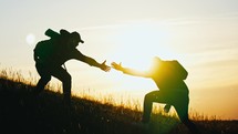 Silhouette of a helping hand to the man mountaineer. Two hikers on top of the mountain, a man helps a man to climb. Two hiker helping on hiking trail to summit the top of mountain. Teamwork concept.