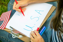 a girl writing USA on paper on a clipboard 