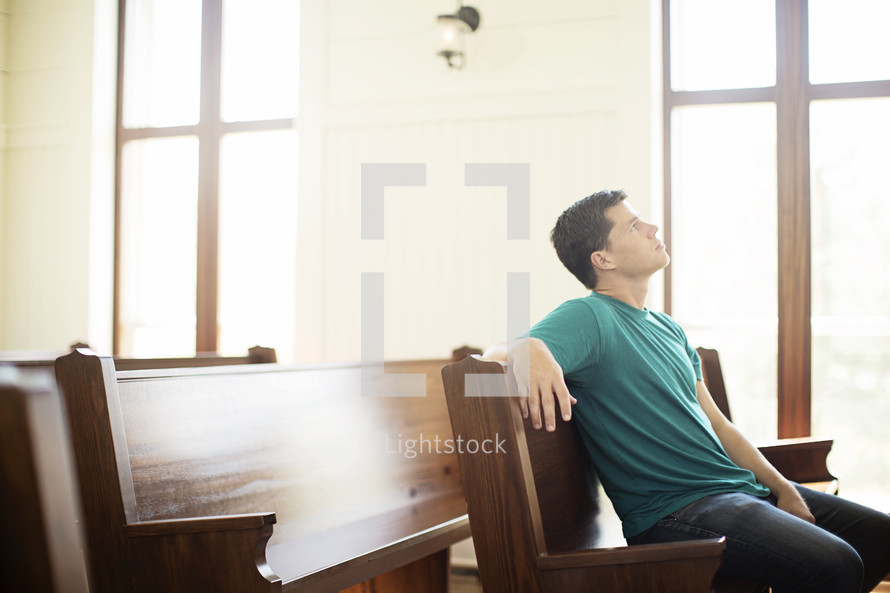 Man looking up while praying in a church pew.