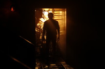 silhouette of a man standing in a dark room and the glow of sunlight behind him 