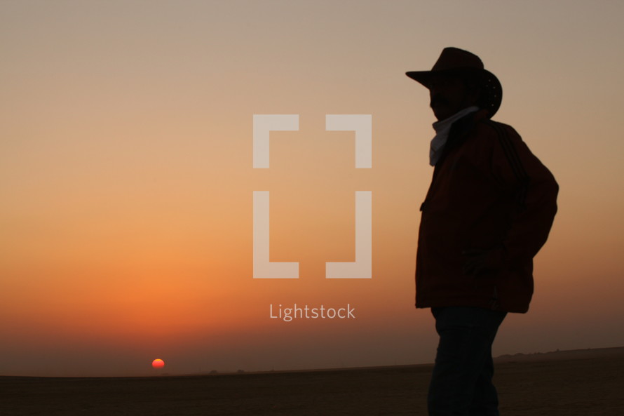 silhouette of a cowboy standing in a desert at sunset 