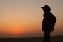silhouette of a cowboy standing in a desert at sunset 