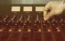A hand turning knobs on a sound board.