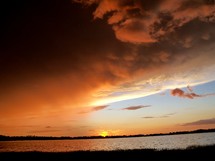 the sun setting against a lake in central Florida with heavy clouds rolling in the sky