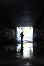 a man walking through a dark wet tunnel 