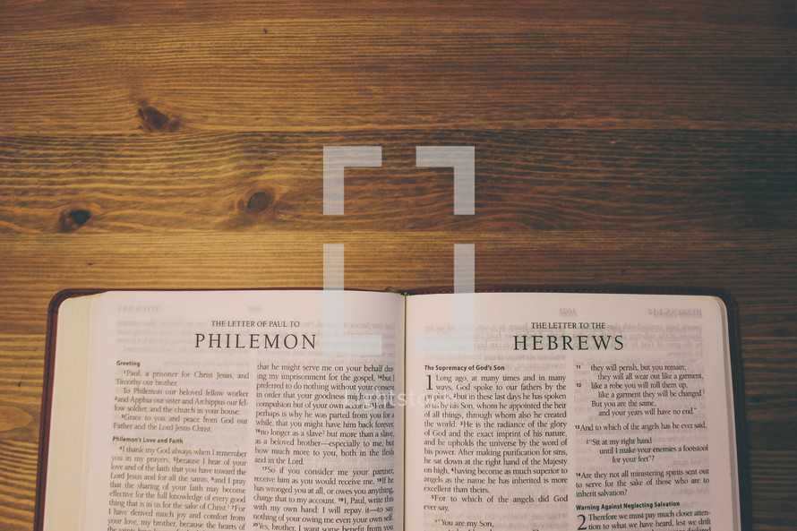 Bible on a wooden table open to the Letter of Paul to Philemon and the Letter to the Hebrews. 