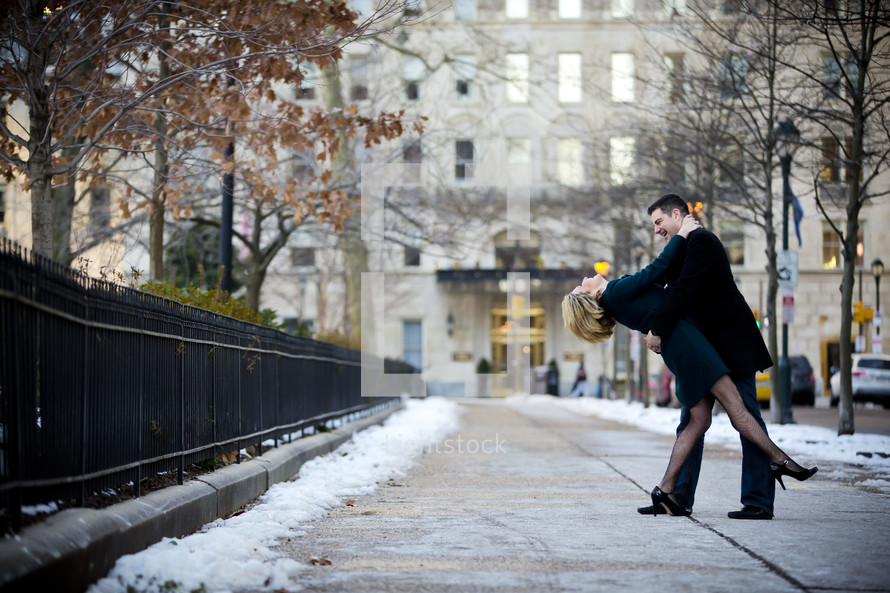 Man holding a woman while standing on the sidewalk with snow.