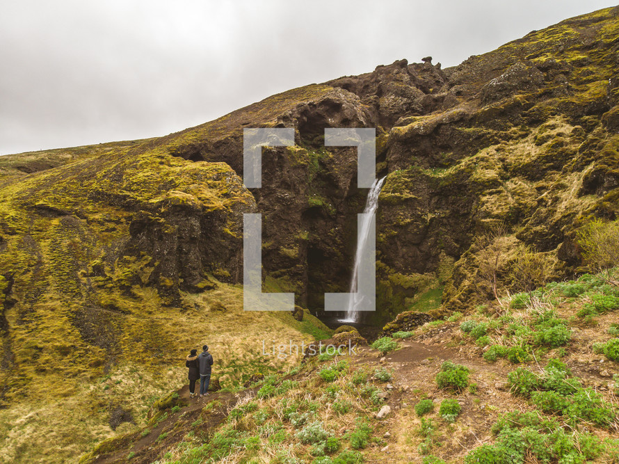 couple watching a waterfall on a green mountainside 
