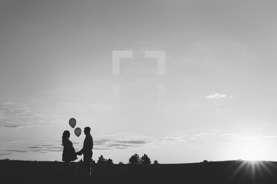 silhouettes of pregnant wife holding hands with her husband while holding balloons