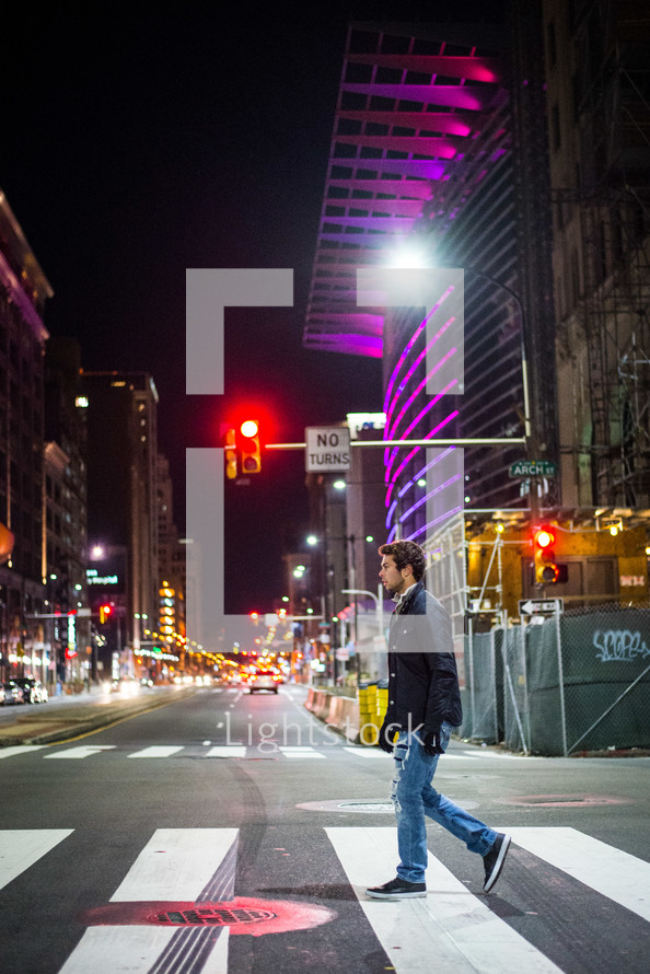 a man crossing a city street on a crosswalk at night 