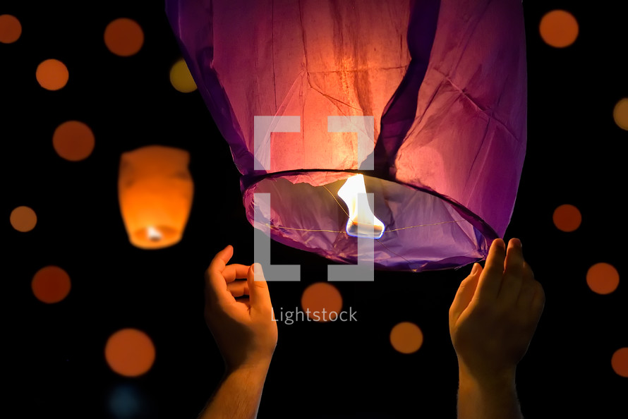 Hands of tourist launching sky lantern to the sky. Lampions in the dark