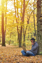 Man with laptop and smartphone in forest, autumn colors, sunset warm light