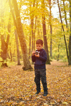 Creative child, kid photographer (a little boy) with a camera taking pictures of colorful autumn forest