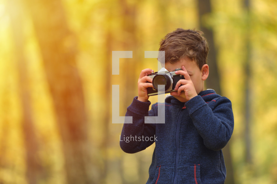 Creative child, kid photographer (a little boy) with a camera taking pictures of colorful autumn forest