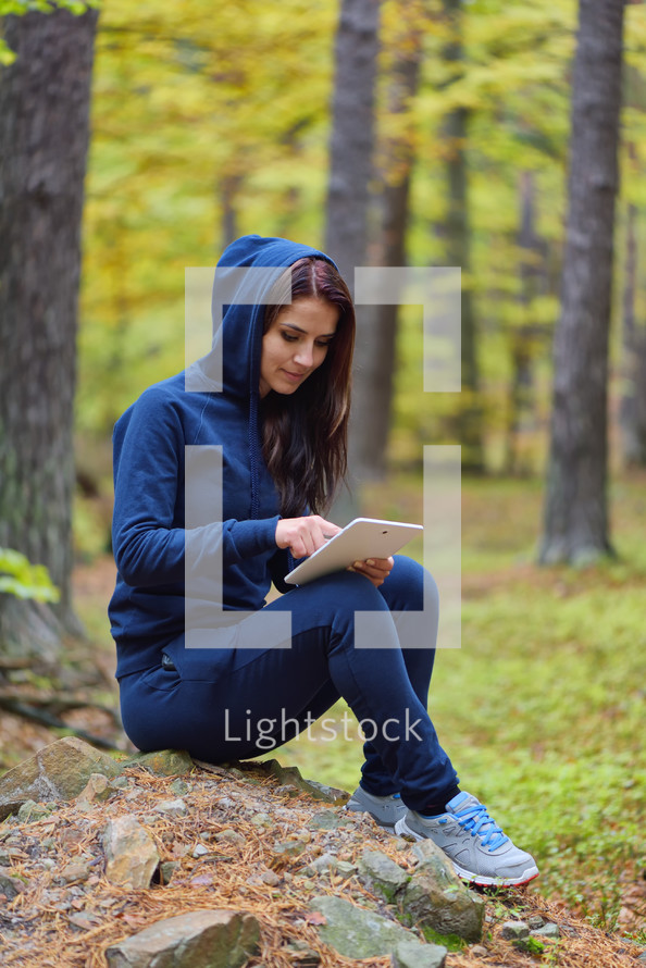 a woman sitting in a forest looking at a tablet screen 