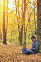 man with laptop in forest, autumn colors, sunset warm light