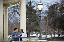 Embracing couple standing outside on a balcony by a lamppost. 