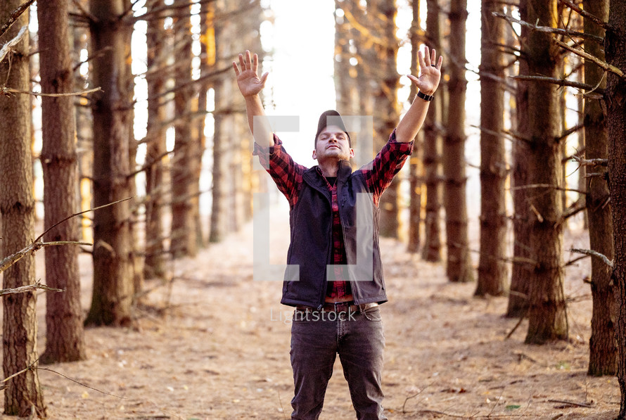 a man standing outdoors in the woods with hands raised 