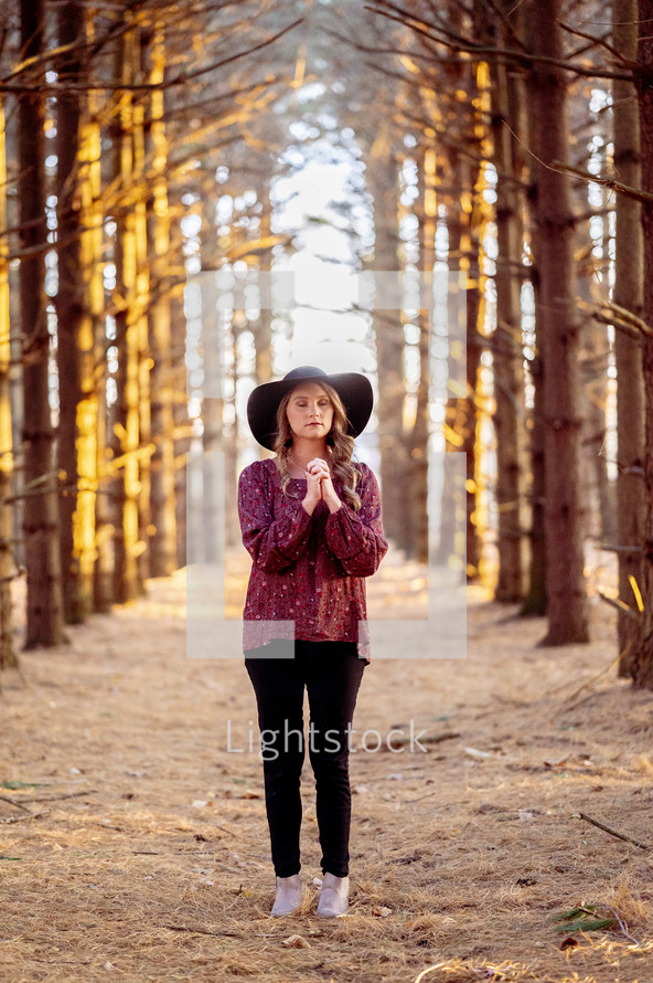 a woman standing in a forest alone praying 