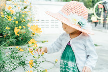 a little girl in a sunhat standing next to flowers 
