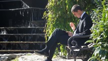 man using a tablet sitting on a bench 