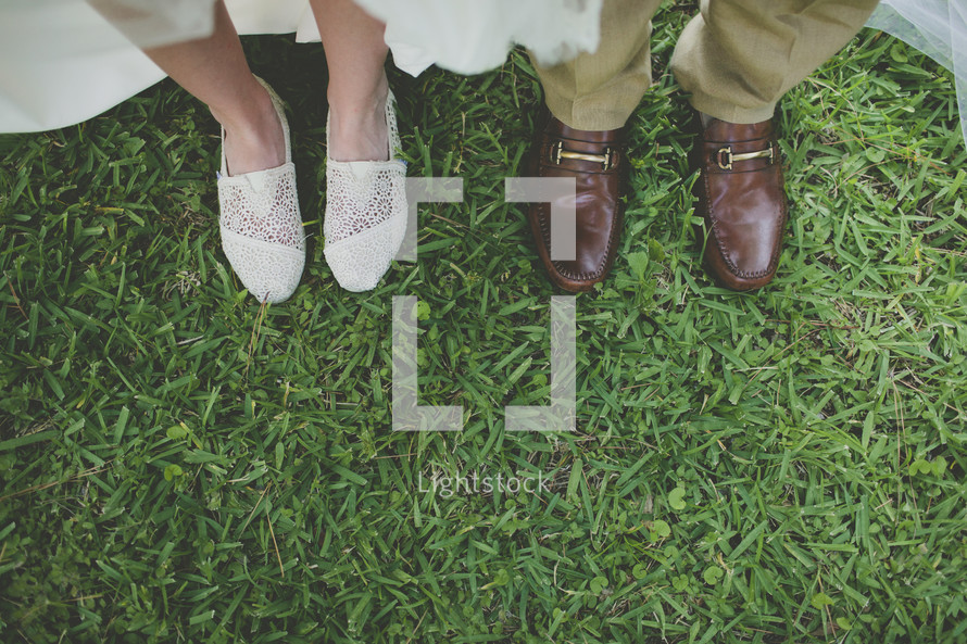 two pairs of feet in shoes standing in the grass after their wedding
