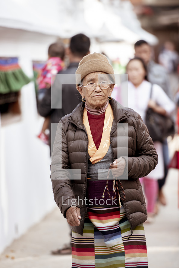 elderly woman walking with prayer beads in Tibet 