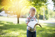 a toddler standing outdoors reading a Bible 