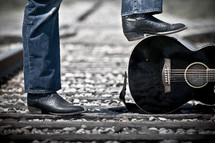 man standing on train tracks with a guitar 