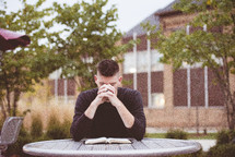man praying over an opened Bible outdoors 