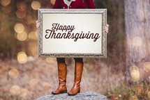 a woman holding a sign the reads Happy Thanksgiving 