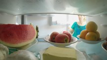 POV shot from inside a refrigerator of a woman opening the door and taking out food