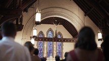 A group of people stand in church pews during a catholic ceremony or mass looking at Jesus on the cross.