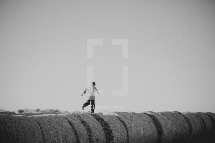 A young boy running on  bales of hay