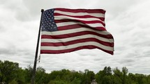 Slow motion shot of America flag waving in the wind on cloudy day.