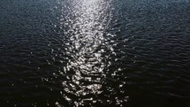 Slow-motion of dark and dramatic body of water with the sun shining bright creating a shimmering light on the water.