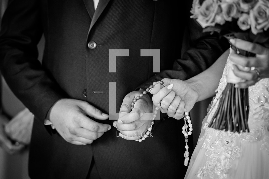 A couple holding a rosary together during a wedding cermony preparations.
