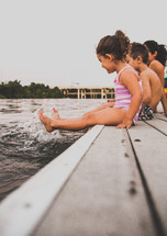 children sitting on a dock with their feet in the water 