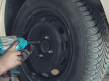 Mechanic changing a car tire in a workshop on a vehicle on a hoist using an electric drill to loosen the bolts in a concept of service or replacement