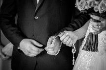 A couple holding a rosary together during a wedding cermony preparations.
