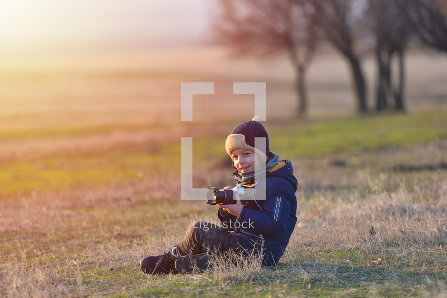 Creative child, kid photographer (a little boy) with a camera taking landscape pictures in warm sunset light
