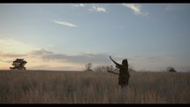 a woman standing in a field holding a guitar with her arms raised 