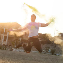 Portrait at sunset of a young man jumping with energy and colored powder.