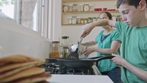 Boy preparing pancakes with his mother for breakfast in the kitchen