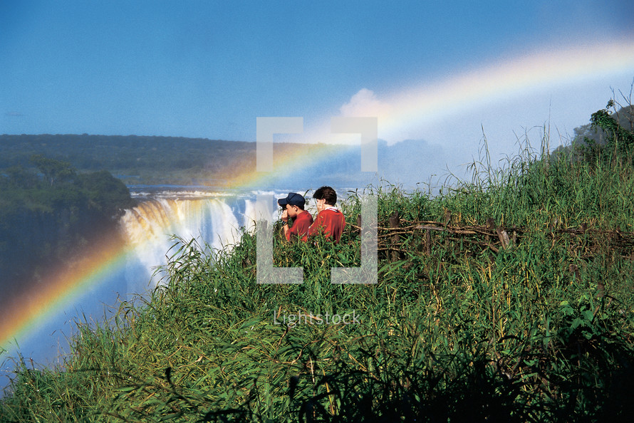People viewing a rainbow over a waterfall