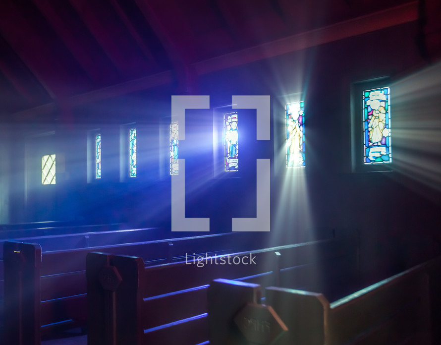 rays of sunlight shining through stained glass windows in onto church pews 