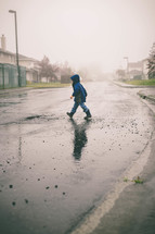 Child n a raincoat crossing the wet street.