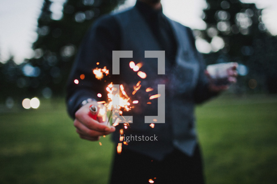 man holding a sparkler and a lighter