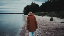a woman walking on a shore in a jacket 