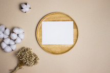 Blank white note on wooden plate with cotton and dried flowers